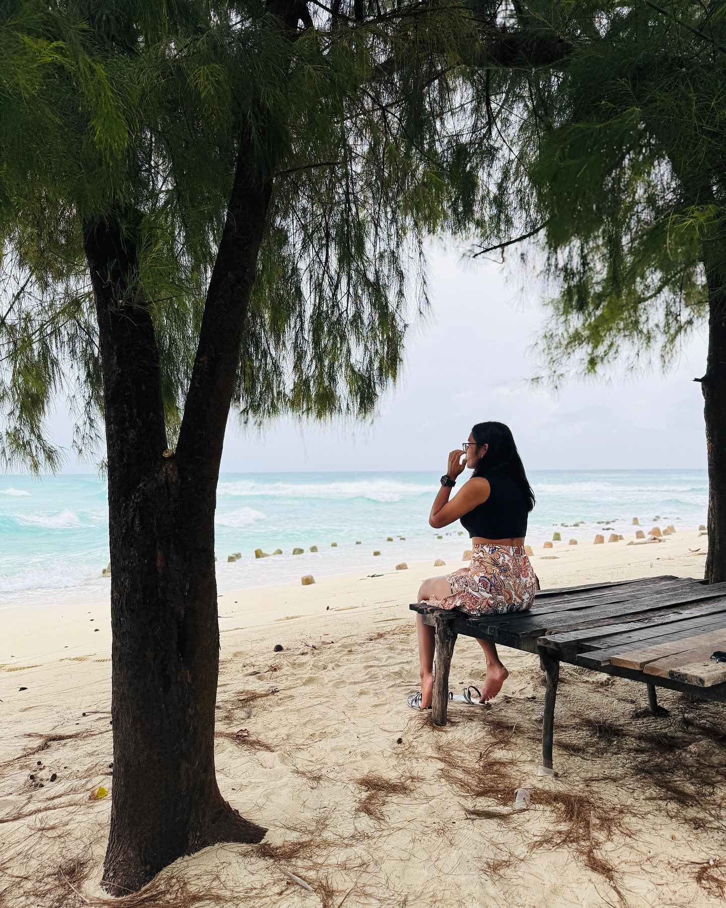 Guest resting on a wooden bench under casuarina trees on a Lakshadweep beach